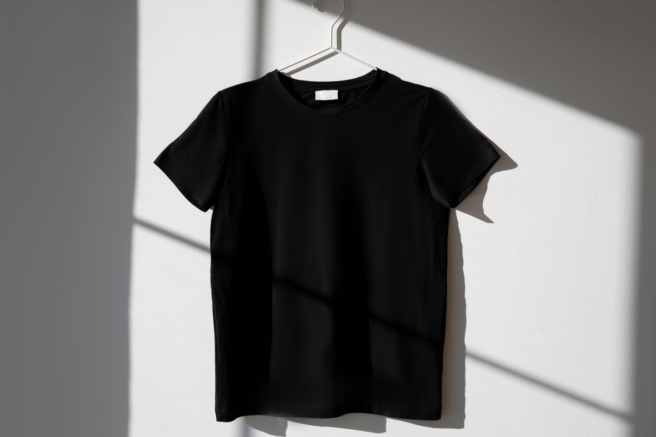 why-choose-us Minimalist image of a black t-shirt on a hanger with dramatic shadows on a white wall.