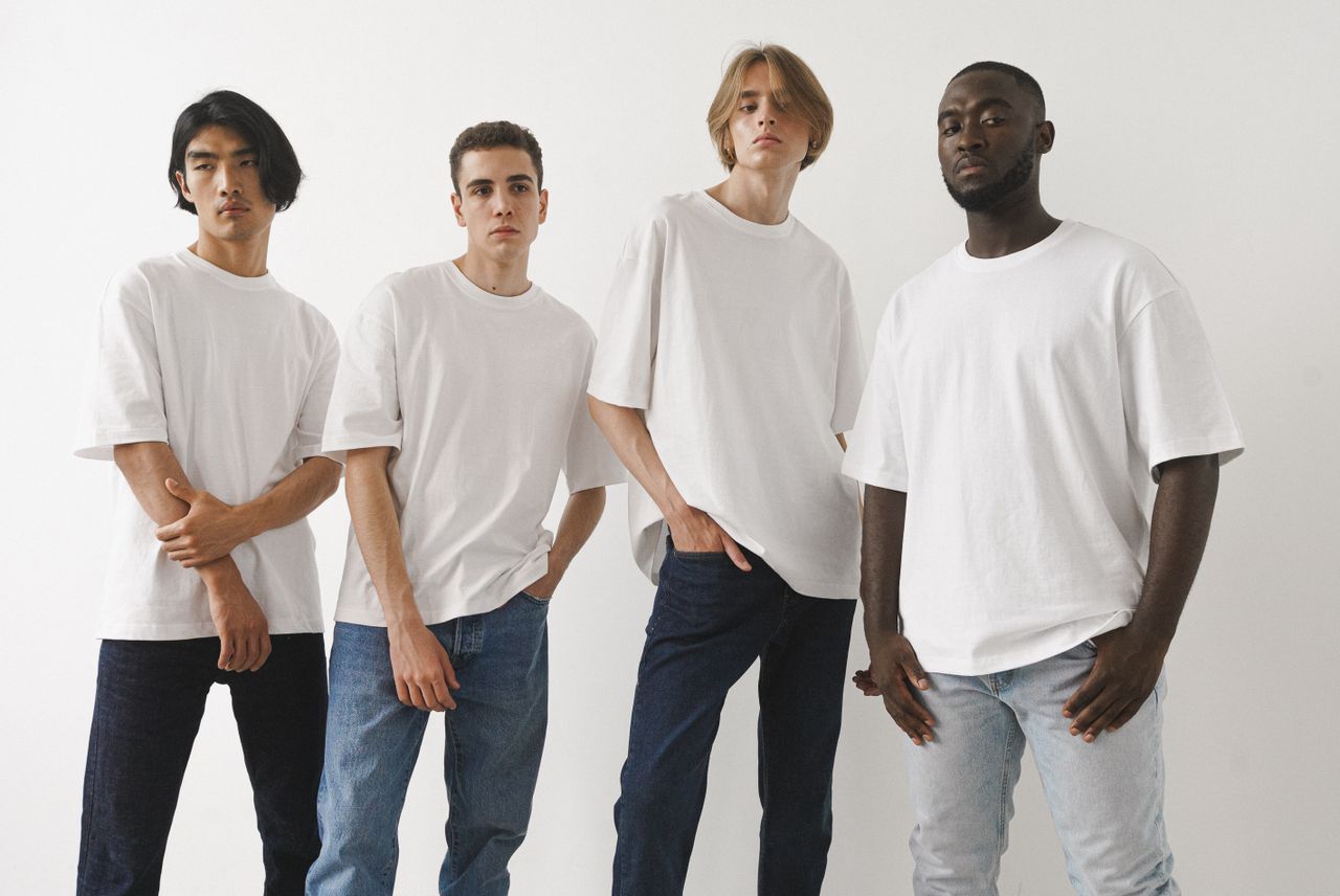 home-hero A group of four diverse men modeling white t-shirts and jeans in a studio setting.